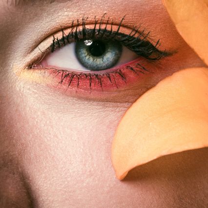 partial view of beautiful young woman with colorful eyeshadows and orange lily flower